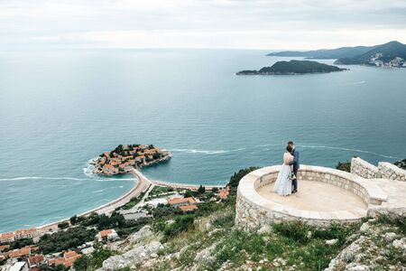 The bride and groom admire a beautiful view of the island of Sveti Stefan in Montenegro.の写真素材