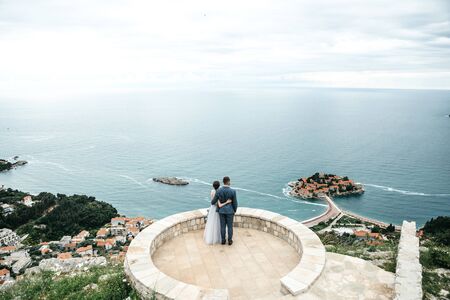 The bride and groom admire a beautiful view of the island of Sveti Stefan in Montenegro.の写真素材