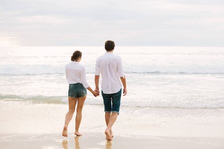A man and woman hold hands and walk along the sand or along the beach by the sea.の写真素材