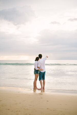 A man hugs a woman. They stand and look at the sea. Solitude together.の写真素材
