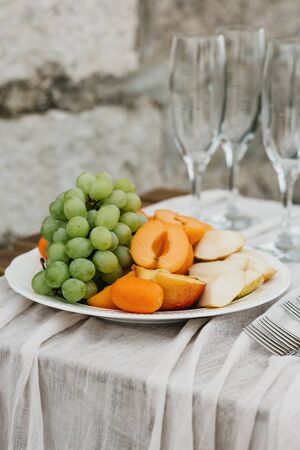 Peaches and grapes on a plate next to empty glasses for wine. Preparation for the celebration.の写真素材