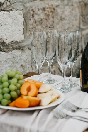 Peaches and grapes on a plate next to empty glasses for wine. Preparation for the celebration.の写真素材