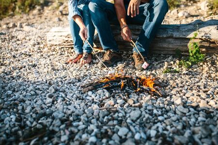 People or a couple prepare or roast marshmallows on a campfire in nature.の写真素材