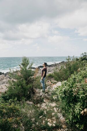 A girl stands on a stone sea shore and admires the sea.の写真素材