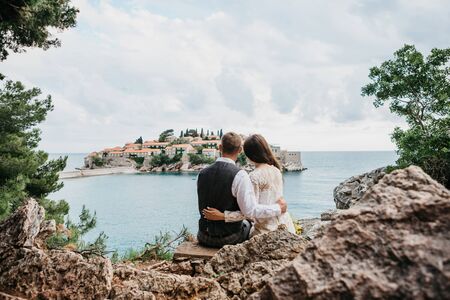 A man and a woman admire a beautiful view of the island of Sveti Stefan in Montenegro. He hugs her.の写真素材