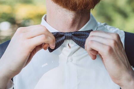 Closeup of mans hand adjusting bow-tie on shirt