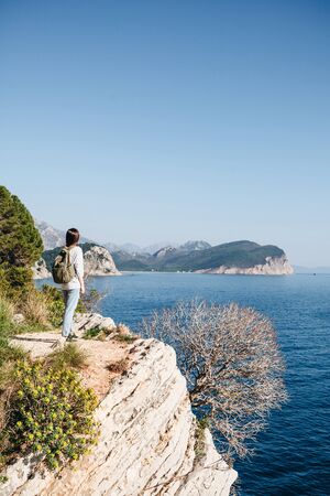 A tourist with a backpack on top of a cliff or hill next to the sea looks into the distance. Travel alone.の写真素材