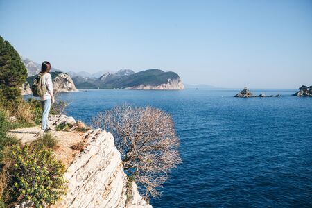 A tourist with a backpack on top of a cliff or hill next to the sea looks into the distance. Travel alone.の写真素材