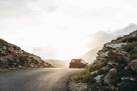 The road on which the car leaves in the middle of the mountainous terrain at sunset. Road trip or adventure.の写真素材
