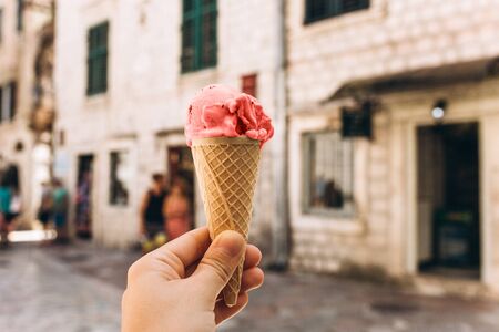 Closeup of girl or woman holding ice cream of trend living coral color in waffle cup on the background of an old city street.の写真素材