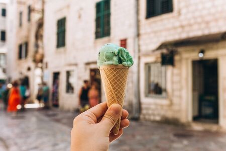 Closeup of a girl holding mint or pistachio ice cream in her hand against the background of a building or an old city streetの写真素材