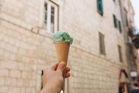 Closeup of a girl holding mint or pistachio ice cream in her hand against the background of a building or an old city streetの写真素材