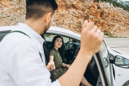A man helps a woman get out of the car. He gave her his hand for this.の写真素材