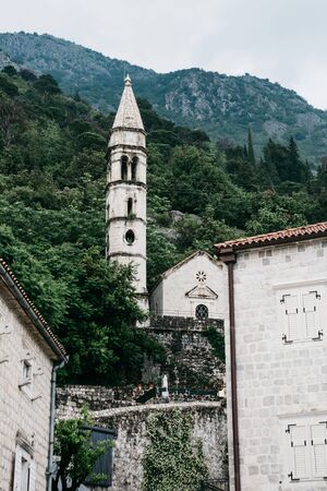 View of the old bell tower and the church in Perast in Montenegro on the background of mountains. Traditional architecture.の写真素材