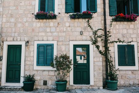 Frontal view of a stone residential building with entrance door and windows with shutters and decorated with plants.の写真素材