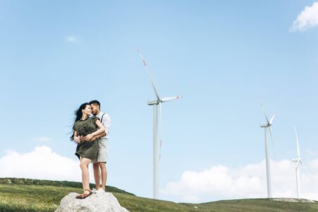 A young couple stands on the background of windmills and hugs. Close relationships and love between...