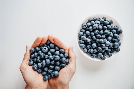 Closeup man holds blueberries in hands on a white background. Near a plate with these berries. Source of vitamins and diet food.の写真素材