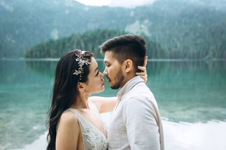 The groom and the bride hug and kiss on the background of the lake. Wedding in nature.の写真素材