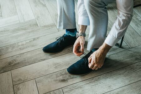 A man in trousers is tying shoelaces on shoes indoors.の写真素材