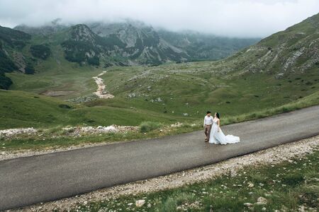The bride and groom are on the road in the highlands. Wedding in the mountains.の写真素材