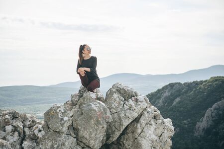 A beautiful young adult girl in solitude is sitting on top of a mountain and she is happy.の写真素材