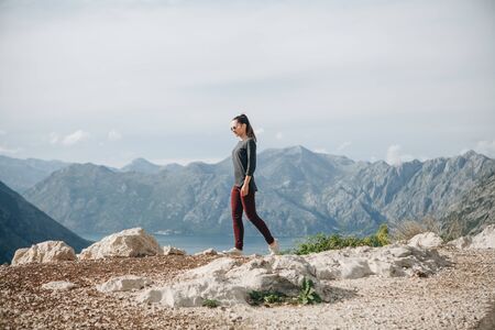 A girl in solitude walks on top of a mountain against the background of other mountainsの写真素材