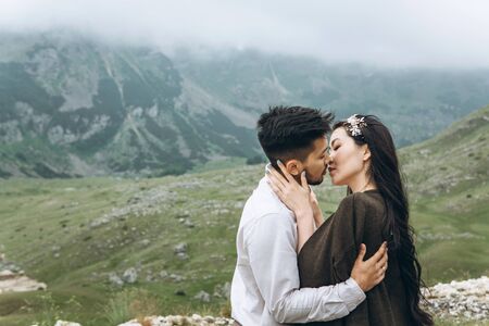 A man gently hugs a woman and they kiss on nature against the backdrop of a mountain landscape.の写真素材