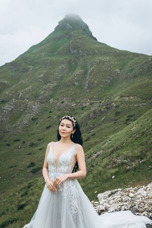 Portrait of a beautiful bride in a traditional white dress on a background of mountain landscape. Outdoor weddingの写真素材