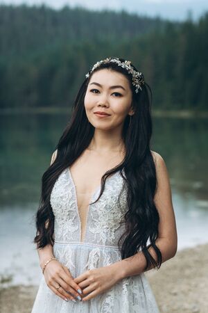Portrait of a beautiful elegant bride in a white traditional dress on a lake backgroundの写真素材