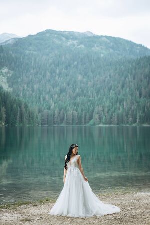 Portrait of a beautiful elegant bride in a white traditional dress on a lake backgroundの写真素材