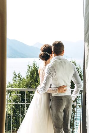 Bride and groom stand and hug on the balcony and look at the beautiful landscape.の写真素材