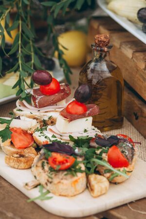 Close up of sandwiches with cheese and meat and other food and a bottle of olive oil on the table.の写真素材