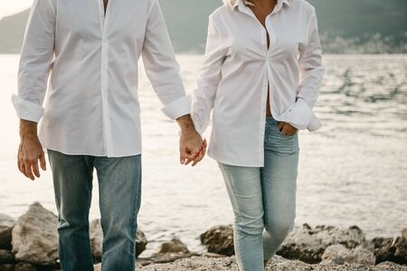 The couple holds hands and walks on the shore near the sea.の写真素材