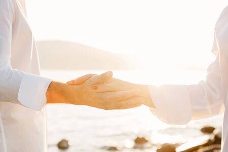 A man and a woman hold each others hands on the background of the sea and sunset. Close relationships and love and support of each other.の写真素材