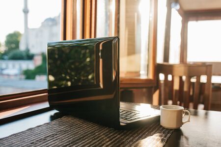 A laptop on a table near the window. Next to a mug with fresh morning fragrant tea or coffee. Home office or work remotely or freelance.の写真素材