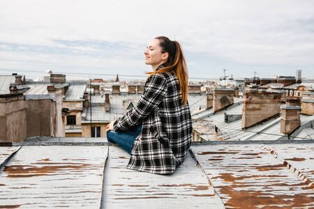 A girl on the roof of a house in solitude meditates or enjoys life or a digital detox. The search for the soul.の写真素材