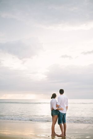 A man hugs a woman. They stand and look at the sea. Solitude together.の写真素材