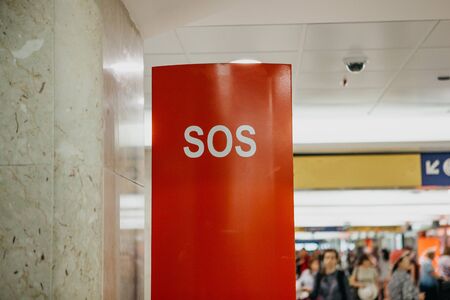 SOS sign on a special stand or booth with a phone for a call at the railway station. Unrecognizable blurry people in the background.の写真素材