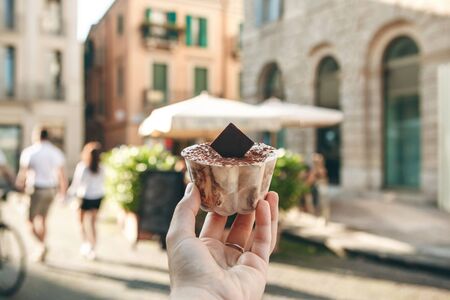 A girl holds in her hand a traditional Italian dessert tiramisu against the background of a street in Verona in Italy.の写真素材