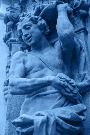 Close-up ancient sculpture of a giant from mythology or another character on the facade of the building in trendy classic blue color.の写真素材
