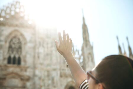 The girl raised her hand to the sunlight and the Duomo Cathedral in Milan in Italy.の写真素材