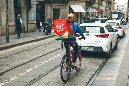Italy, Milan, May 30, 2019: The food deliveryman is cycling along the street in heavy traffic.のeditorial素材