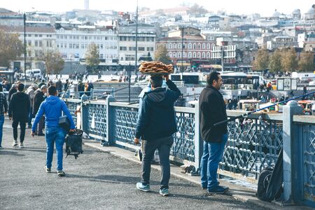 Turkey, Istanbul, December 29, 2019 - The seller walks along the Galata bridge and bears on his head many traditional Turkish bagels Simit. Street food business.のeditorial素材