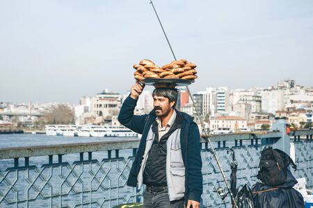 Turkey, Istanbul, December 29, 2019 - The seller walks along the Galata bridge and bears on his head...