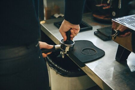 Barista presses ground coffee using tamper. Close-up view on hands with portafilterの写真素材