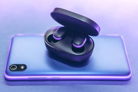 The wireless headphones in the box are unpacked and the cell phone on a trendy neon color gradient background.の写真素材