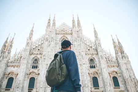 A tourist or student with a backpack looks at the sights in Milan in Italy. He admires the Duomo Cathedral in the town square.の写真素材