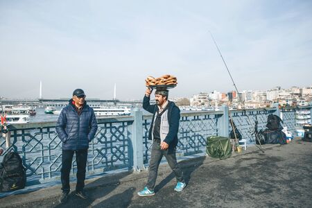Turkey, Istanbul, December 29, 2019 - The seller walks along the Galata bridge and bears on his head many traditional Turkish bagels Simit. Street food business.のeditorial素材