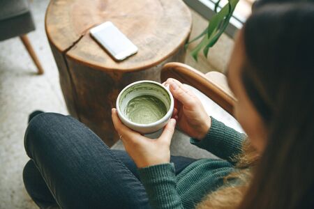 Girl drinks aromatic fresh and healthy green matcha latte tea in a cafe.の写真素材