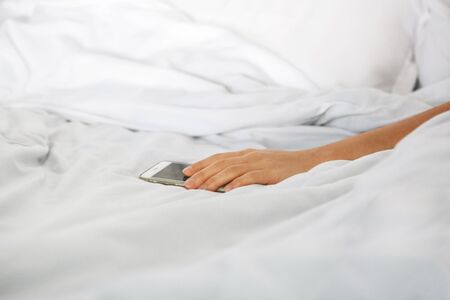 Close-up hand holds the phone in bed. The girl fell asleep with a phone in her hand and she is...
